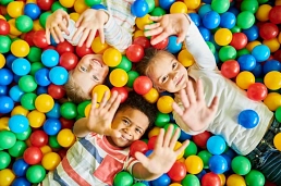 Drei Kinder liegen in einem bunten Bällebad und winken in die Kamera.&nbsp;&copy;&nbsp;Canva / Getty Images Pro