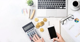 Schreibtisch mit Laptop, Taschenrechner, Münzen, Smartphone und Diagrammen.&nbsp;&copy;&nbsp;Canva